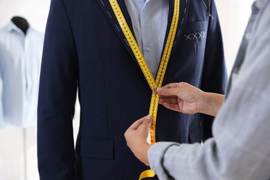 Photo of Tailor measuring jacket on man during fitting in atelier, closeup