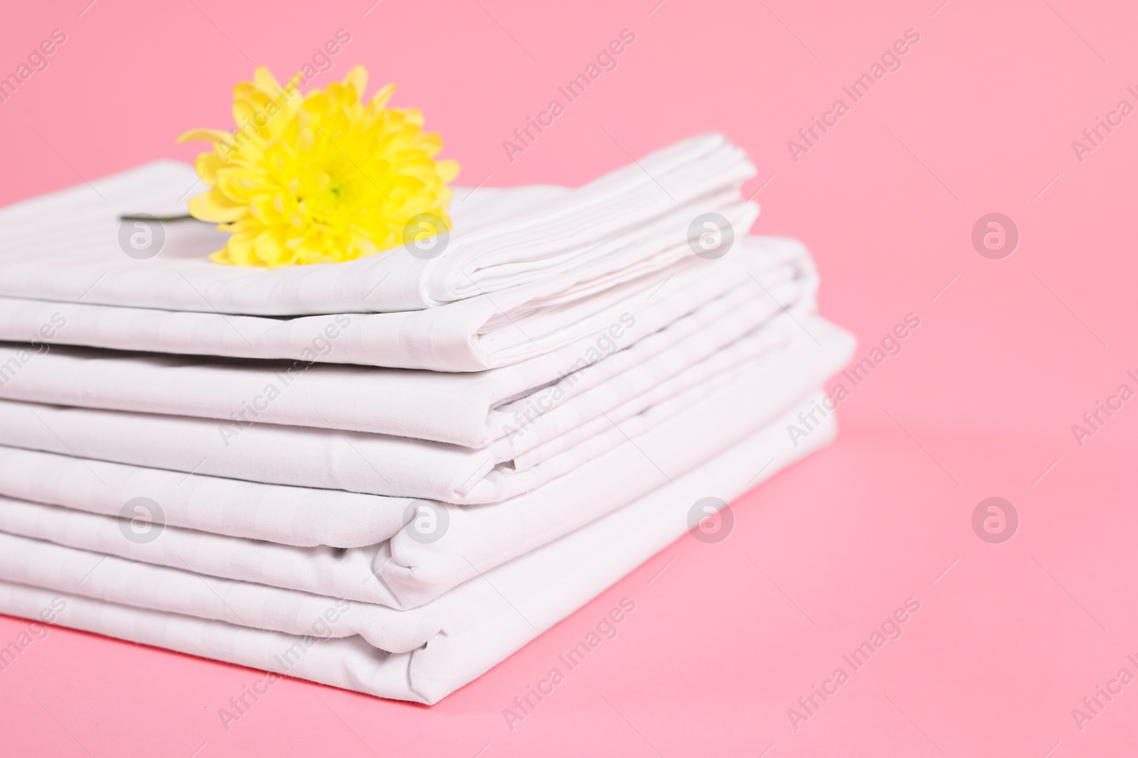 Photo of Stack of clean bed linens and beautiful flower on pink background, closeup