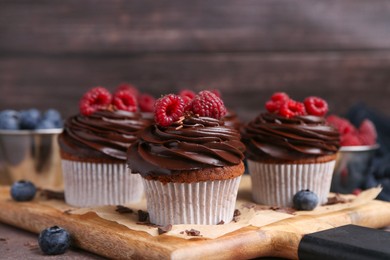 Photo of Tasty cupcakes with chocolate cream and berries on brown table, closeup