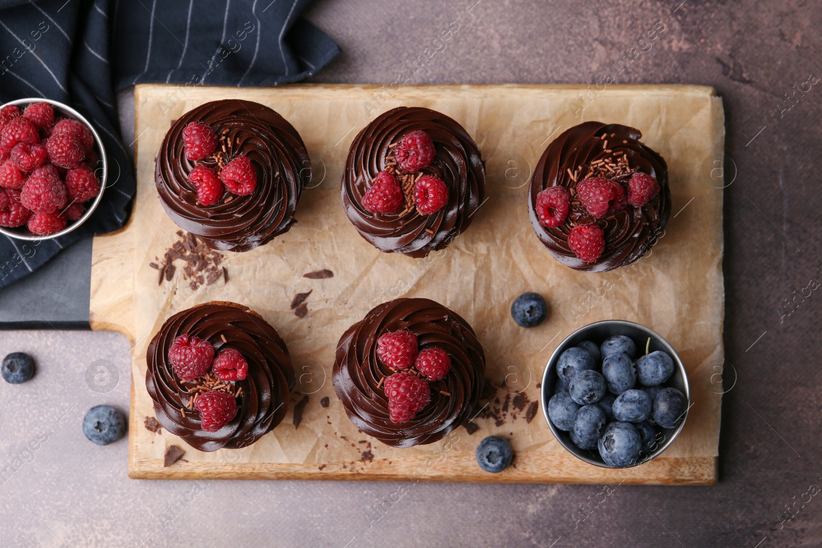 Photo of Tasty cupcakes with chocolate cream and berries on brown table, flat lay