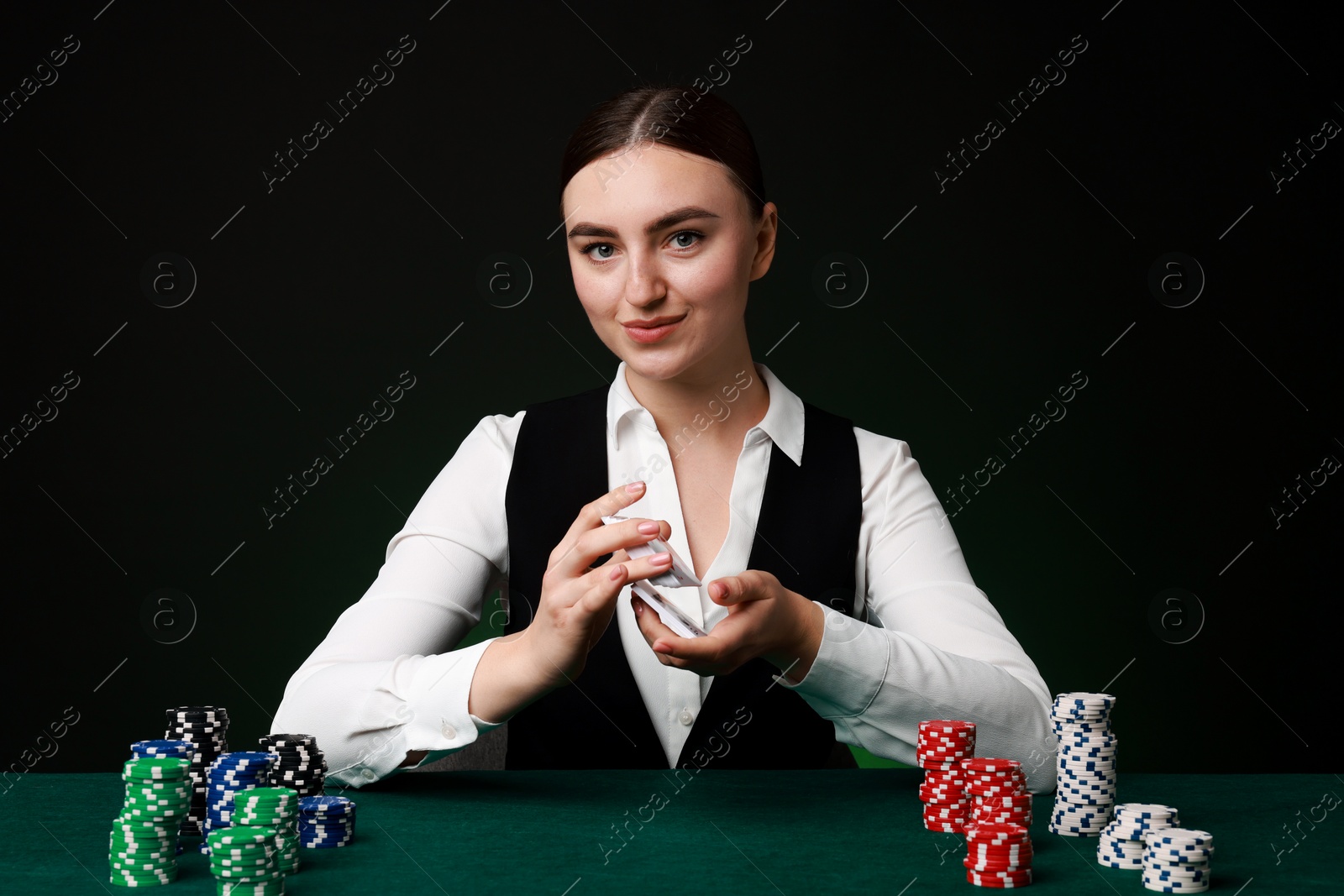 Photo of Professional croupier with chips shuffling playing cards at gambling table on color background