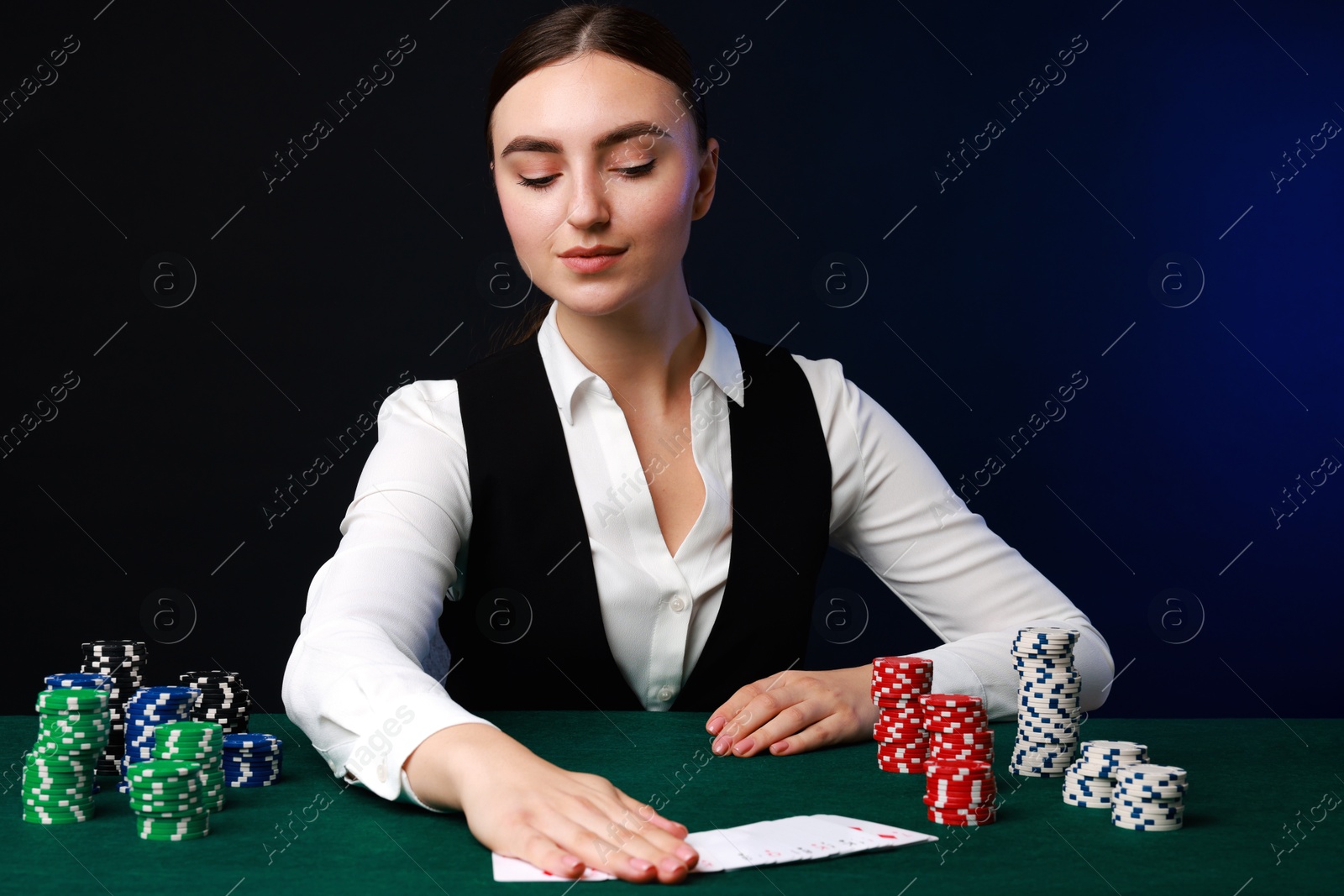 Photo of Professional croupier with casino chips and playing cards at gambling table on color background with smoke