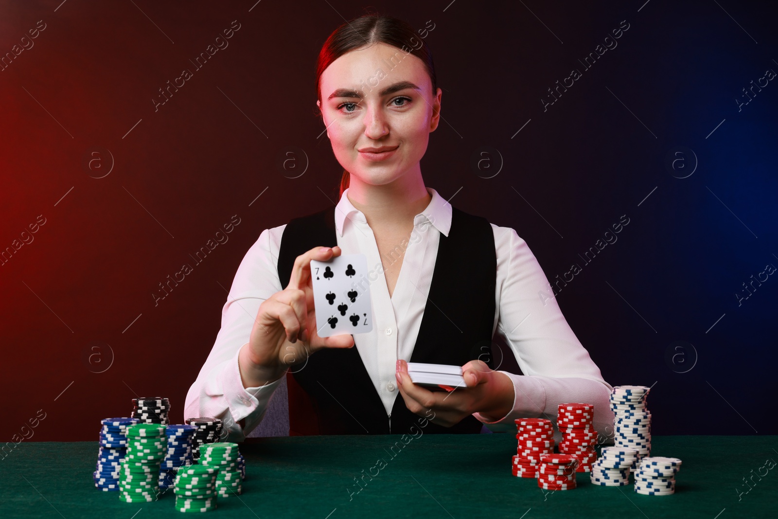 Photo of Professional croupier with casino chips and playing cards at gambling table on color background