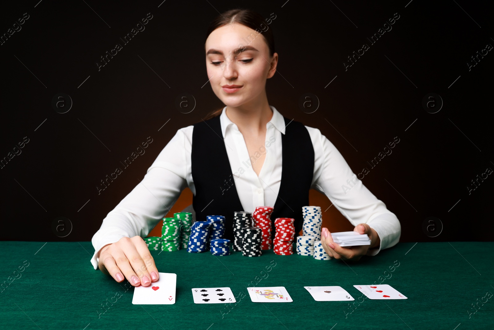 Photo of Professional croupier with casino chips and playing cards at gambling table on color background