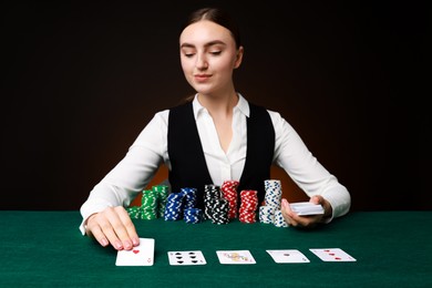 Professional croupier with casino chips and playing cards at gambling table on color background