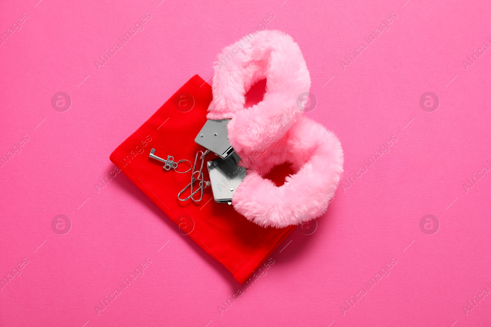 Photo of Fluffy handcuffs, key and bag on pink background, top view