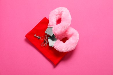 Photo of Fluffy handcuffs, key and bag on pink background, top view