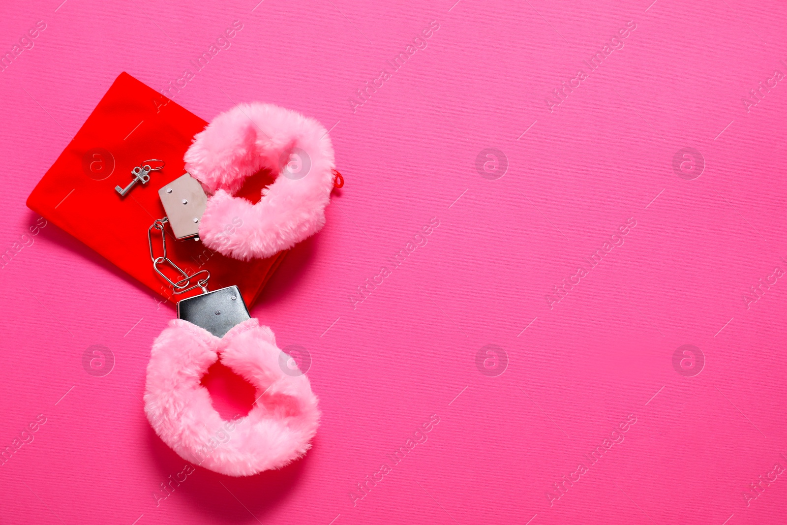 Photo of Fluffy handcuffs, key and bag on pink background, top view. Space for text