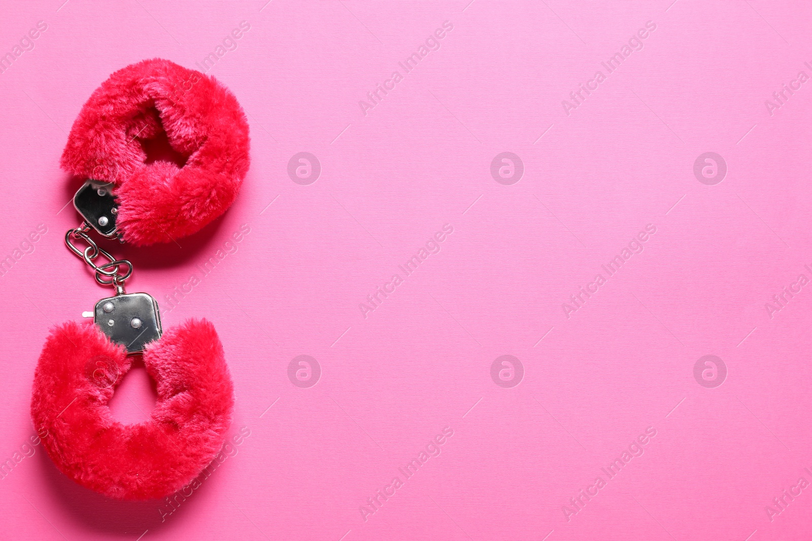 Photo of Fluffy handcuffs on pink background, top view. Space for text