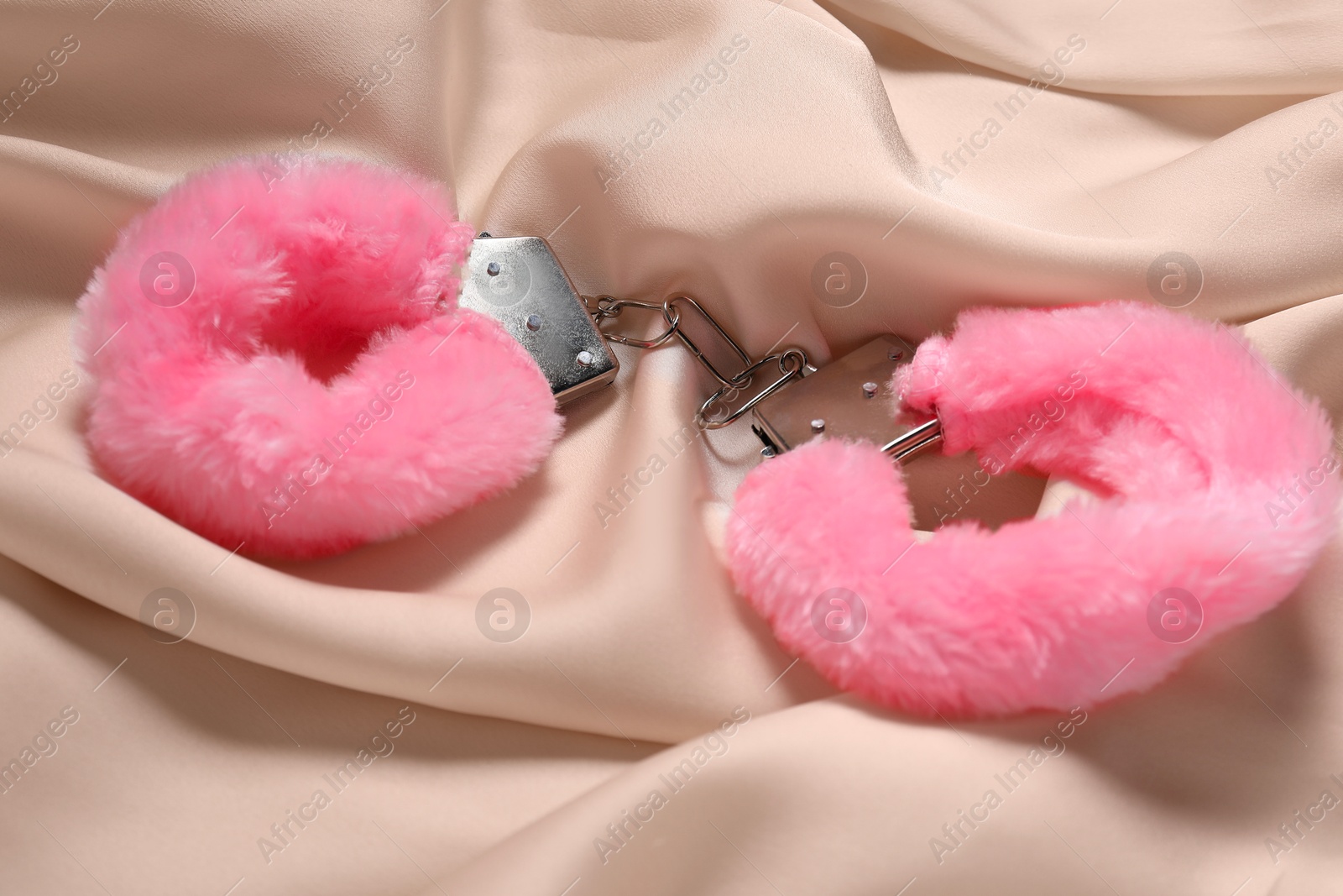 Photo of Pink fluffy handcuffs on beige fabric, closeup