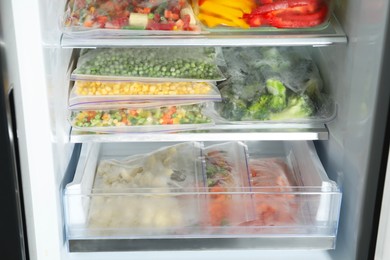 Photo of Plastic bags and glass container with different frozen vegetables in refrigerator