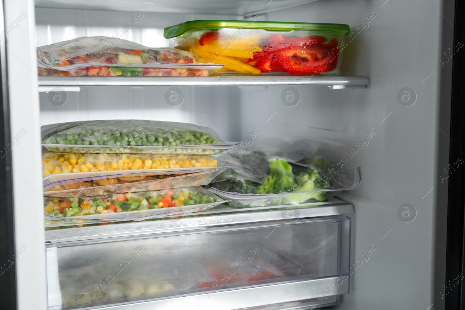 Photo of Plastic bags and glass container with different frozen vegetables in refrigerator