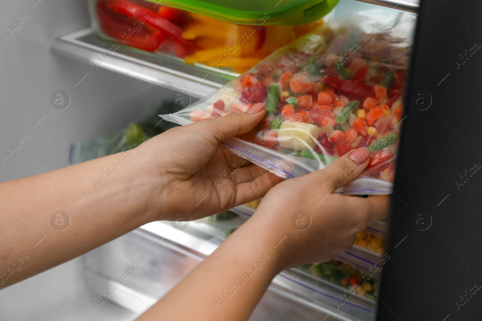 Photo of Woman taking plastic bag with mix of frozen vegetables from refrigerator, closeup