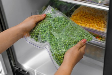 Photo of Woman taking plastic bag with frozen green peas from refrigerator, closeup