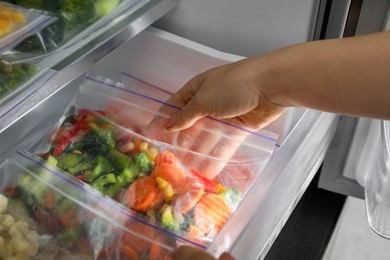 Photo of Woman taking plastic bag with mix of frozen vegetables from refrigerator, closeup