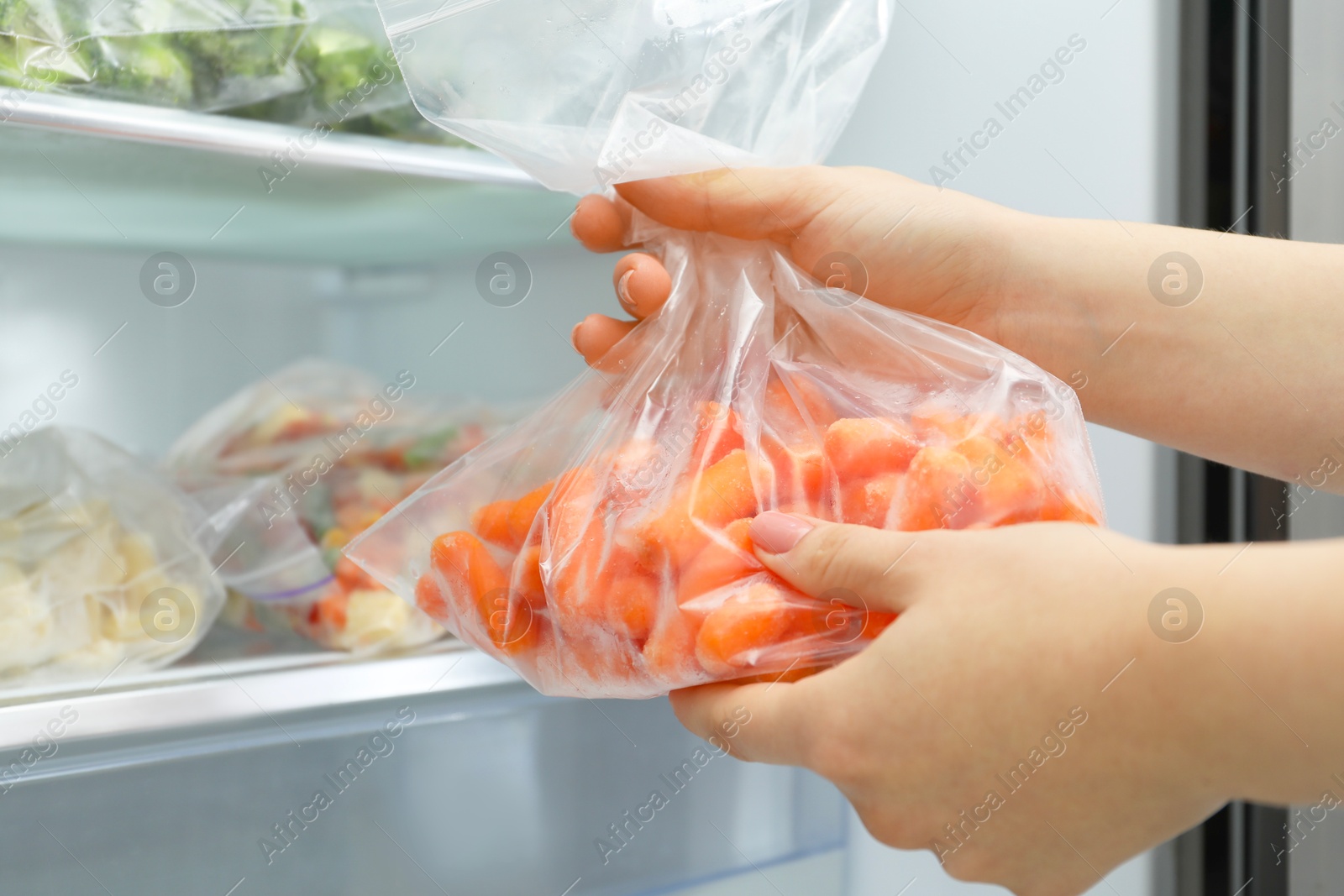 Photo of Woman taking plastic bag with frozen carrots from refrigerator, closeup