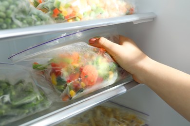 Photo of Woman taking plastic bag with mix of frozen vegetables from refrigerator, closeup