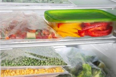 Photo of Plastic bags and glass container with different frozen vegetables in refrigerator, closeup