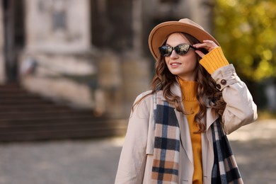 Photo of Charming young woman in stylish outfit on city street, space for text. Autumn season