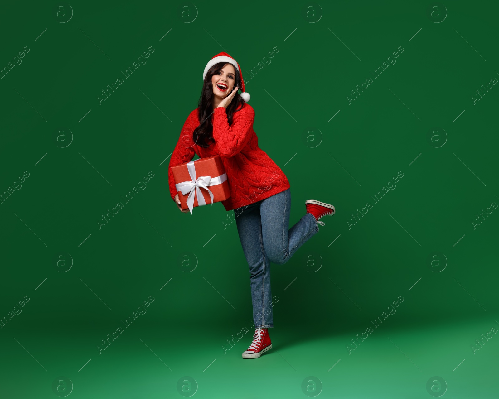 Photo of Attractive woman in Santa hat with Christmas gift on green background