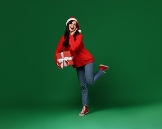 Photo of Attractive woman in Santa hat with Christmas gift on green background