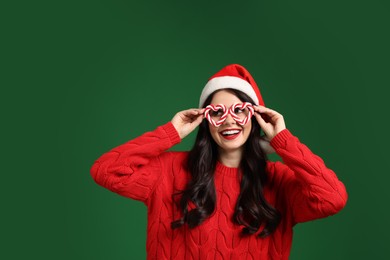 Photo of Beautiful woman in Santa hat and party glasses on green background, space for text. Christmas celebration