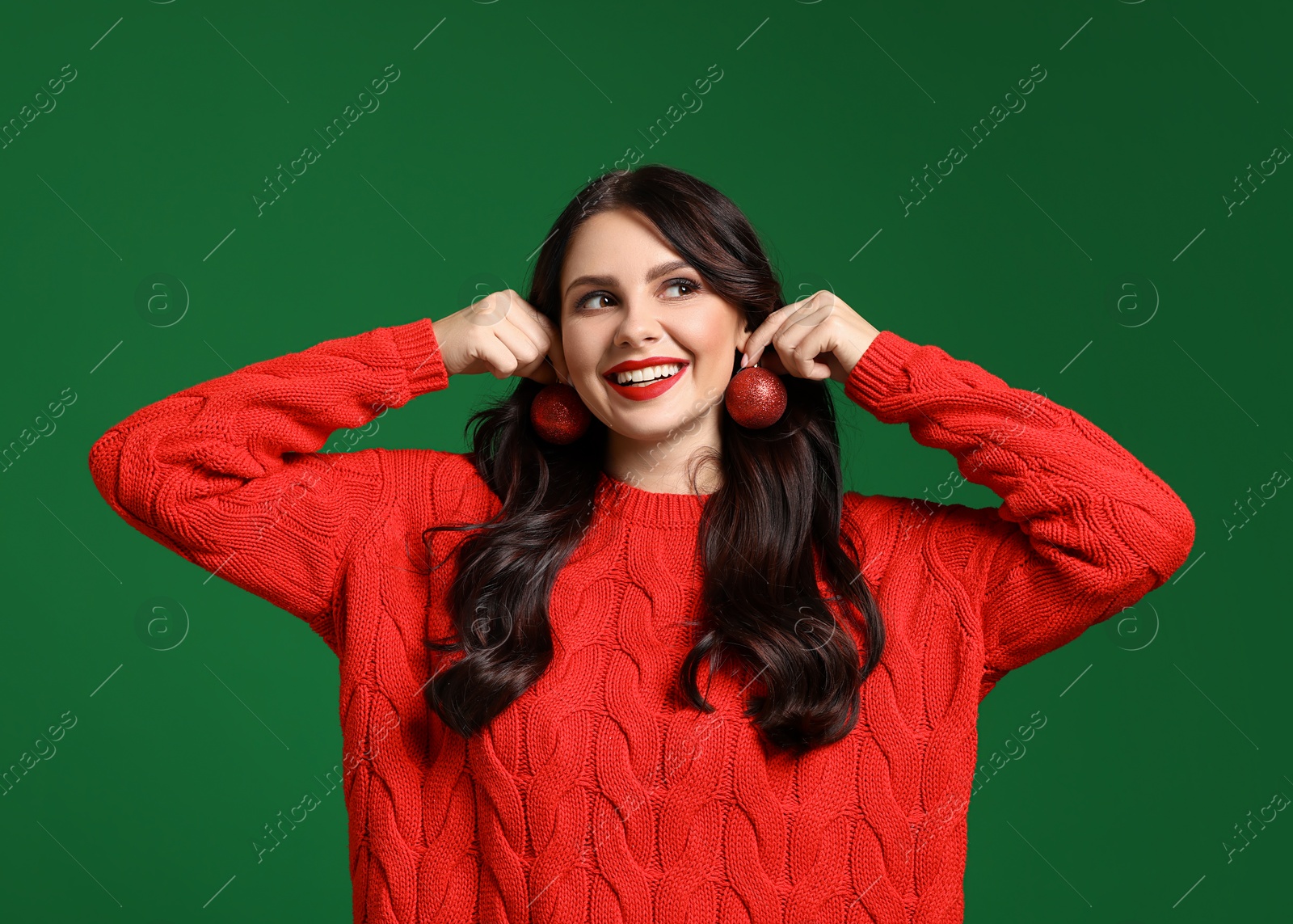 Photo of Happy woman trying Christmas balls as earrings on green background