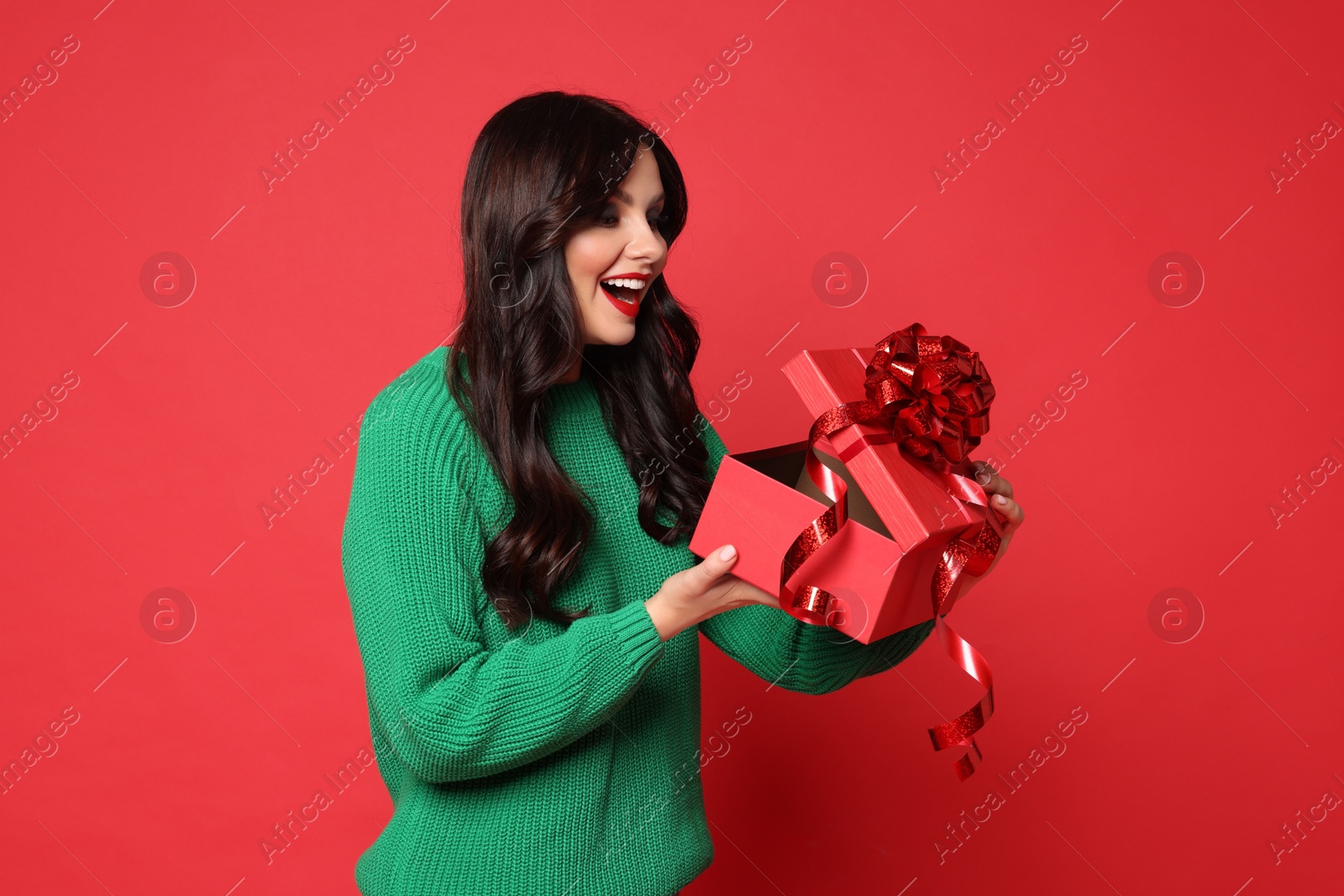 Photo of Beautiful woman opening Christmas gift on red background