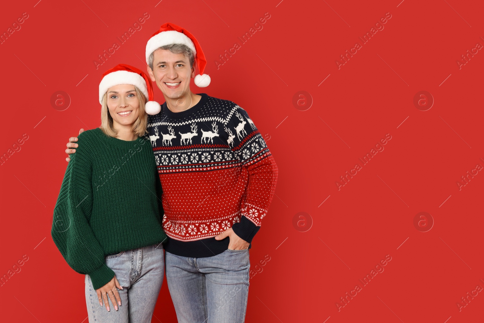 Photo of Happy couple in Santa hats on red background, space for text. Christmas celebration