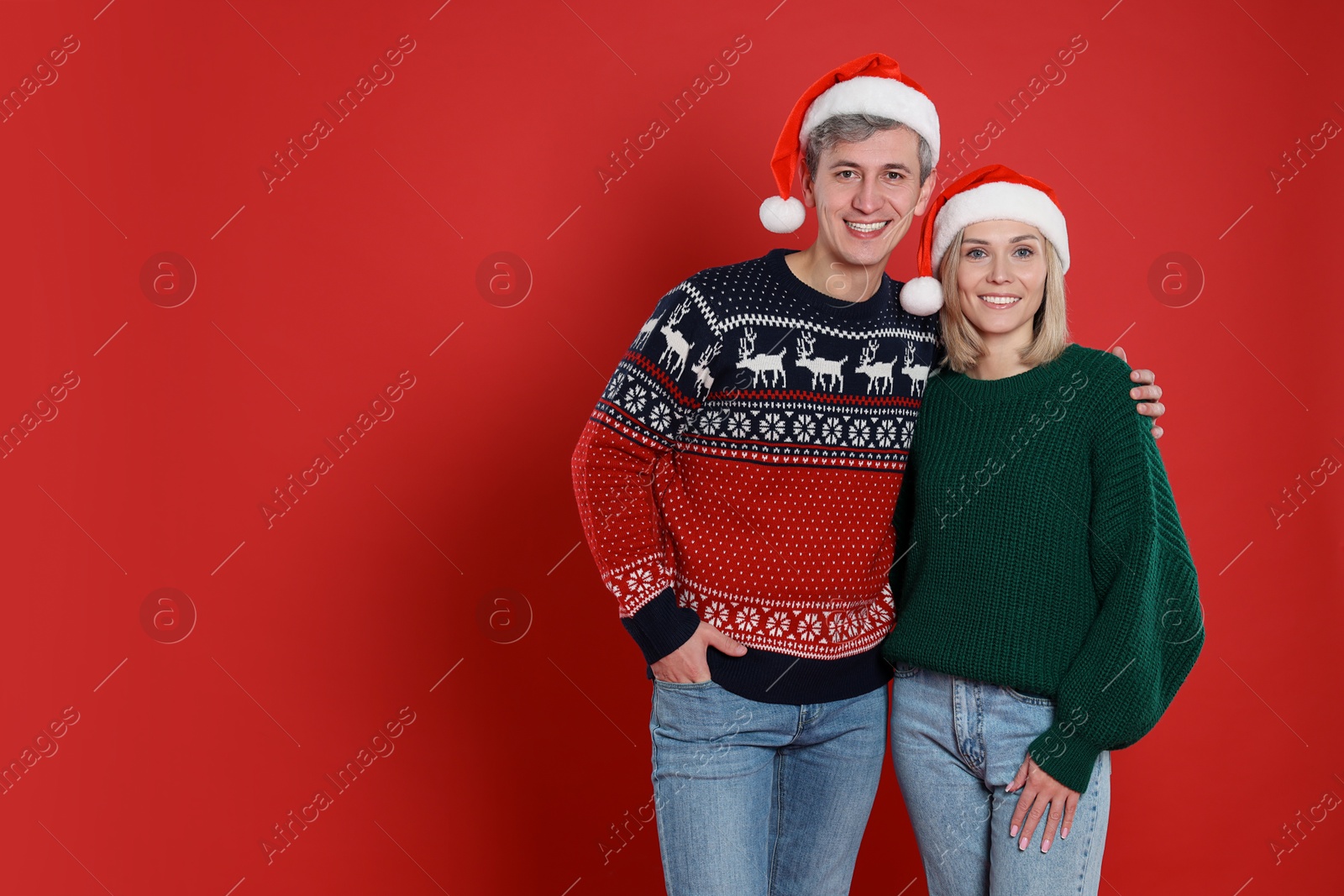 Photo of Happy couple in Santa hats on red background, space for text. Christmas celebration