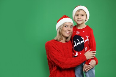 Photo of Mother and son in Santa hats on green background, space for text. Christmas celebration