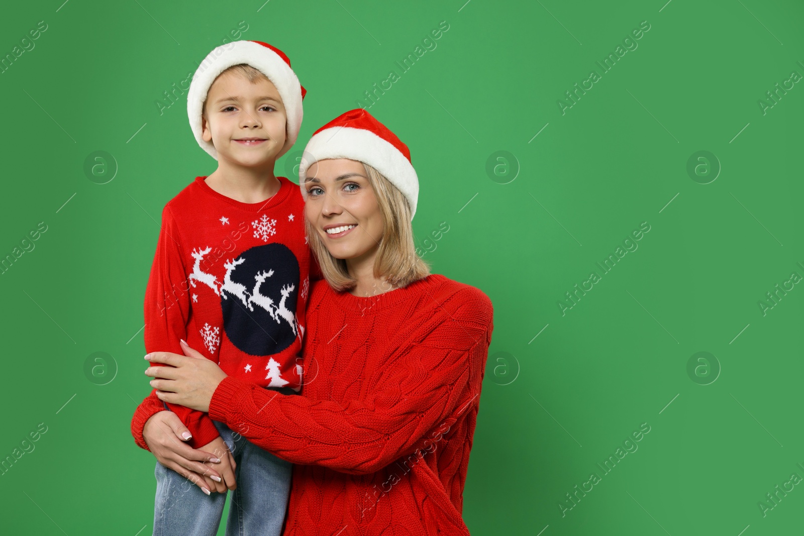 Photo of Mother and son in Santa hats on green background, space for text. Christmas celebration