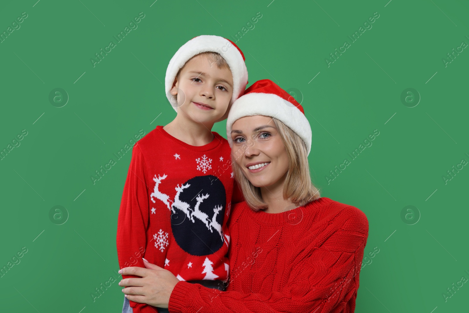 Photo of Mother and son in Santa hats on green background. Christmas celebration