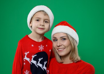 Photo of Mother and son in Santa hats on green background. Christmas celebration