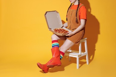 Woman with delicious pizza sitting on step stool against orange background, closeup. Space for text