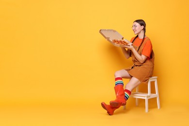 Photo of Beautiful woman with delicious pizza sitting on step stool against orange background, space for text