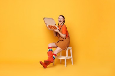 Photo of Beautiful woman with delicious pizza sitting on step stool against orange background