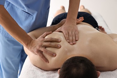 Photo of Professional physiotherapist doing shoulder massage for his client indoors, closeup