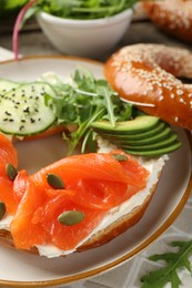 Photo of Delicious bagel with salmon, cream cheese, cucumber, avocado and pumpkin seeds on table, closeup