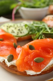 Photo of Delicious bagel with salmon, cream cheese, cucumber and pumpkin seeds on table, closeup