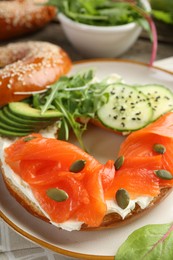 Delicious bagel with salmon, cream cheese, cucumber, avocado and pumpkin seeds on table, closeup