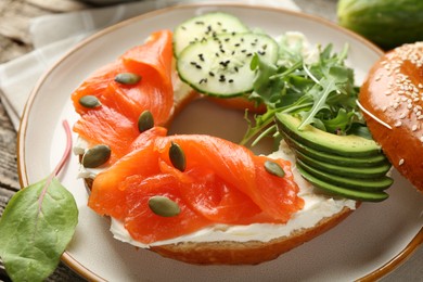 Photo of Delicious bagel with salmon, cream cheese, cucumber, avocado and pumpkin seeds on table, closeup