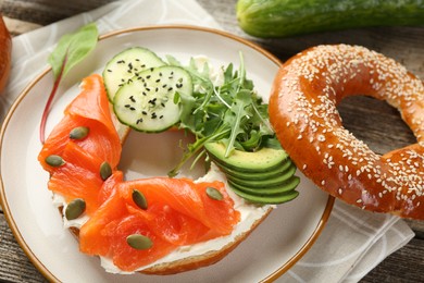 Photo of Delicious bagel with salmon, cream cheese, cucumber, avocado and pumpkin seeds on table, closeup