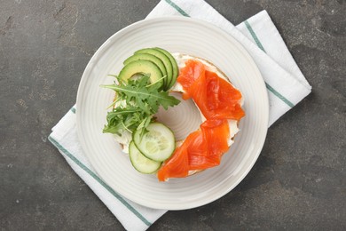 Photo of Delicious bagel with salmon, cream cheese, cucumber and avocado on grey table, top view