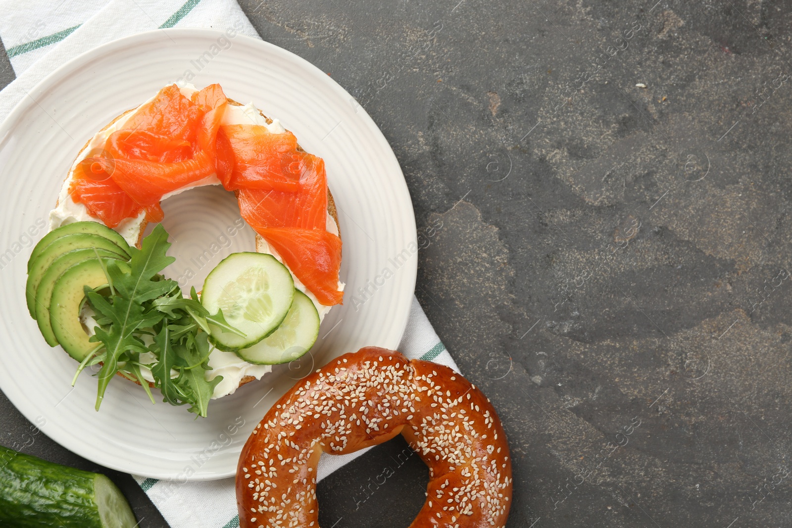 Photo of Delicious bagel with salmon, cream cheese, cucumber and avocado on grey table, flat lay. Space for text