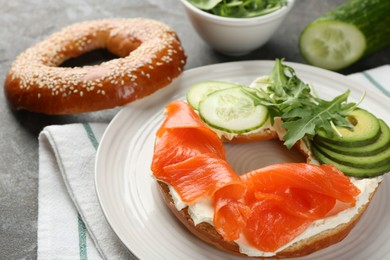 Photo of Delicious bagel with salmon, cream cheese, cucumber and avocado on grey table, closeup