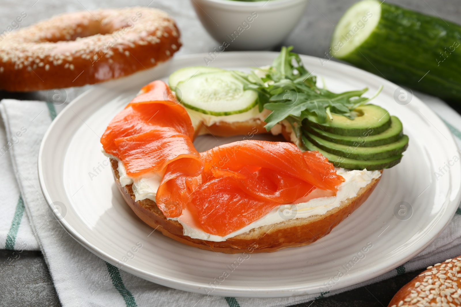 Photo of Delicious bagel with salmon, cream cheese, cucumber and avocado on table, closeup