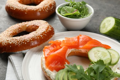 Photo of Delicious bagel with salmon, cream cheese, cucumber and avocado on grey table, closeup