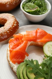 Photo of Delicious bagel with salmon, cream cheese, cucumber and avocado on grey table, closeup