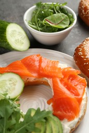 Photo of Delicious bagel with salmon, cream cheese, cucumber and avocado on grey table, closeup